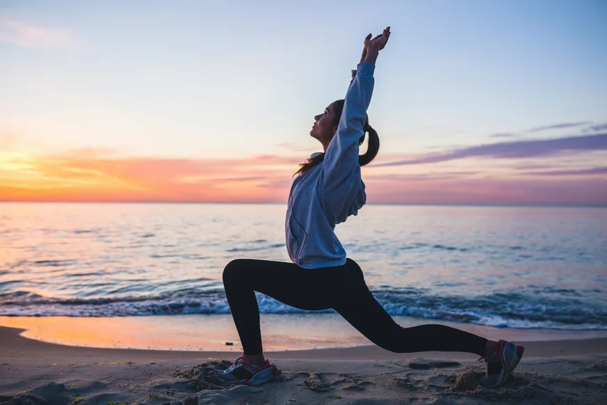 A woman stretching on the beach at sunrise.